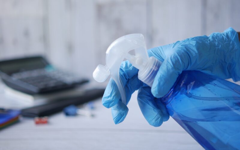 hand in blue rubber gloves holding spray bottle with copy space